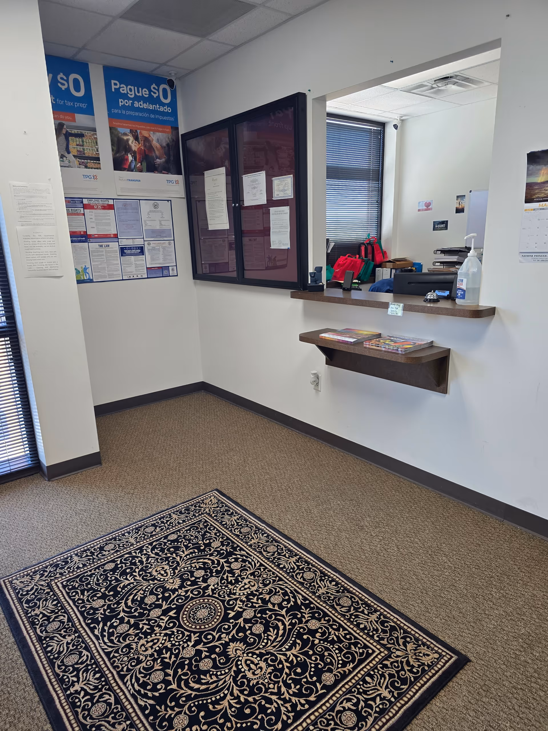 Reception area with a counter, posters, window, and ornate rug.