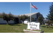 Exterior of a single-story care home with flagpole, sign, and a manicured front lawn.