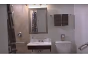 Compact bathroom with sink, mirror, toilet, towels, and accessibility grab bars.