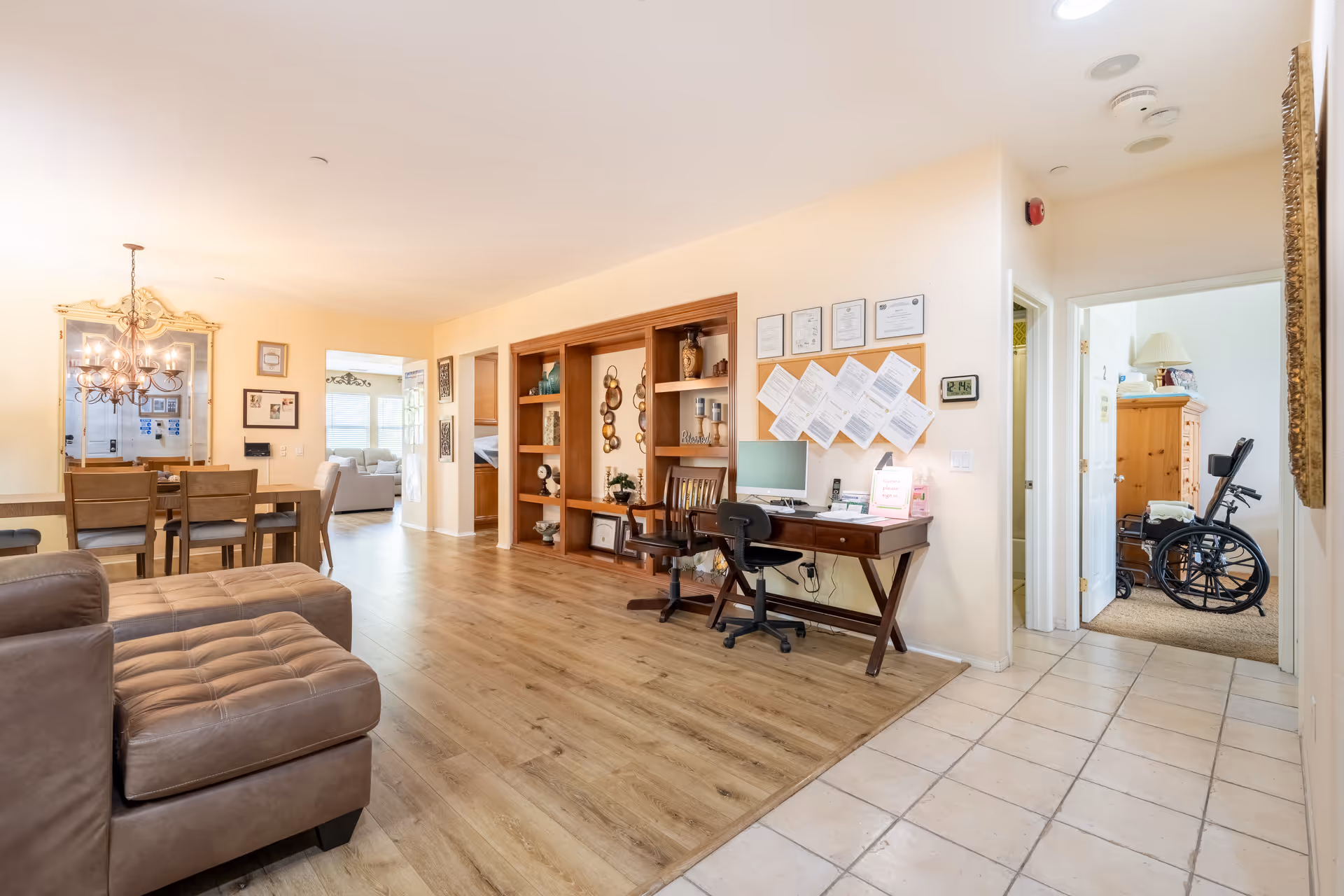 Open, well-lit senior living common area with sofa, desk, dining table, and bookshelf.