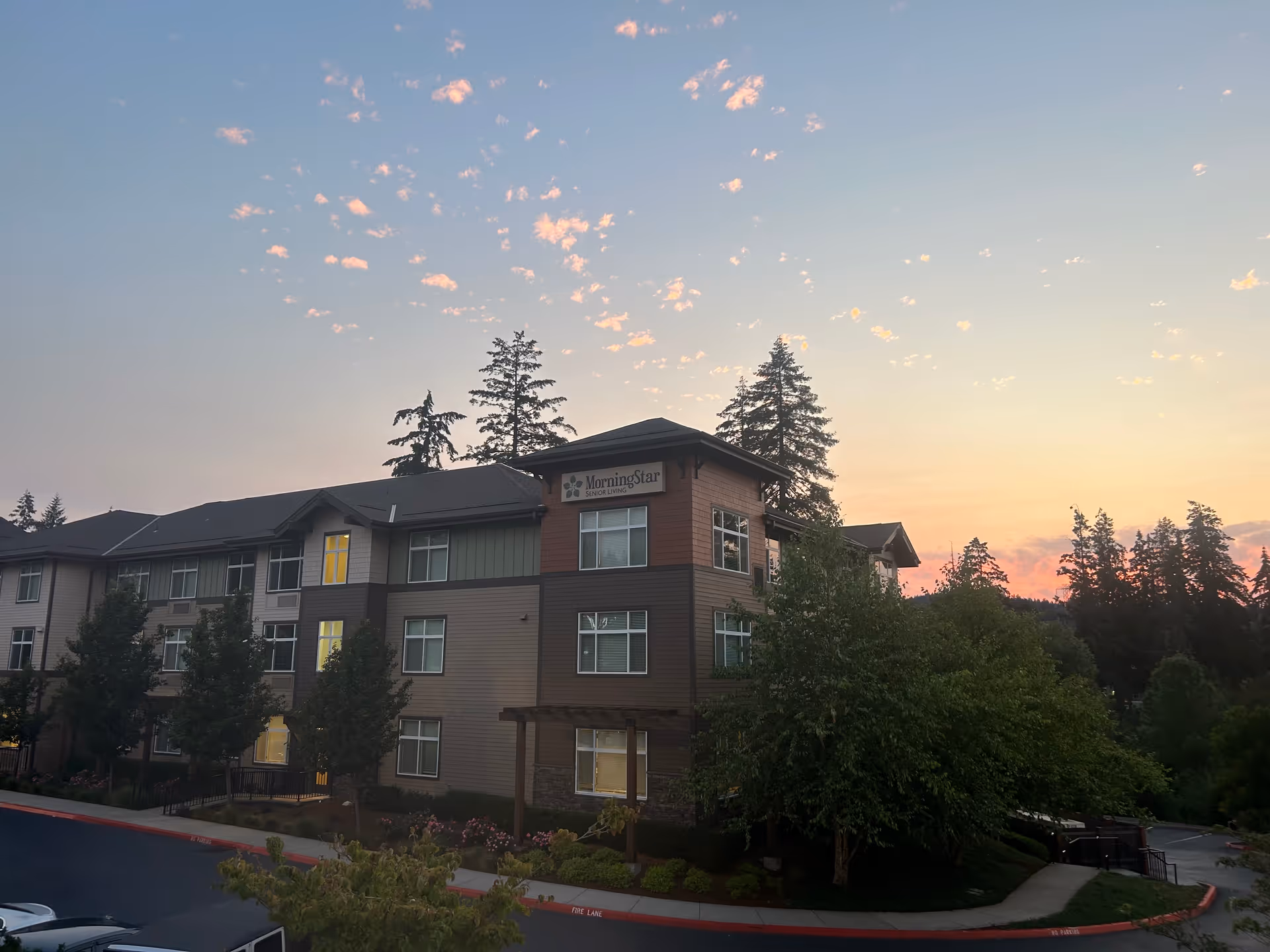 Exterior view of Morning Star of Beaverton senior living building with trees at sunset.