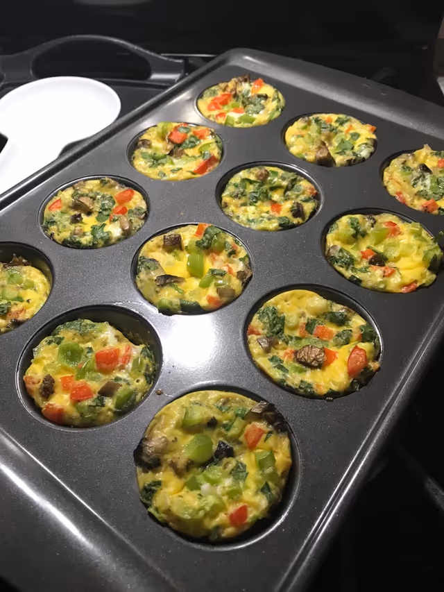 Colorful vegetable egg muffins in a muffin tin on a kitchen counter.