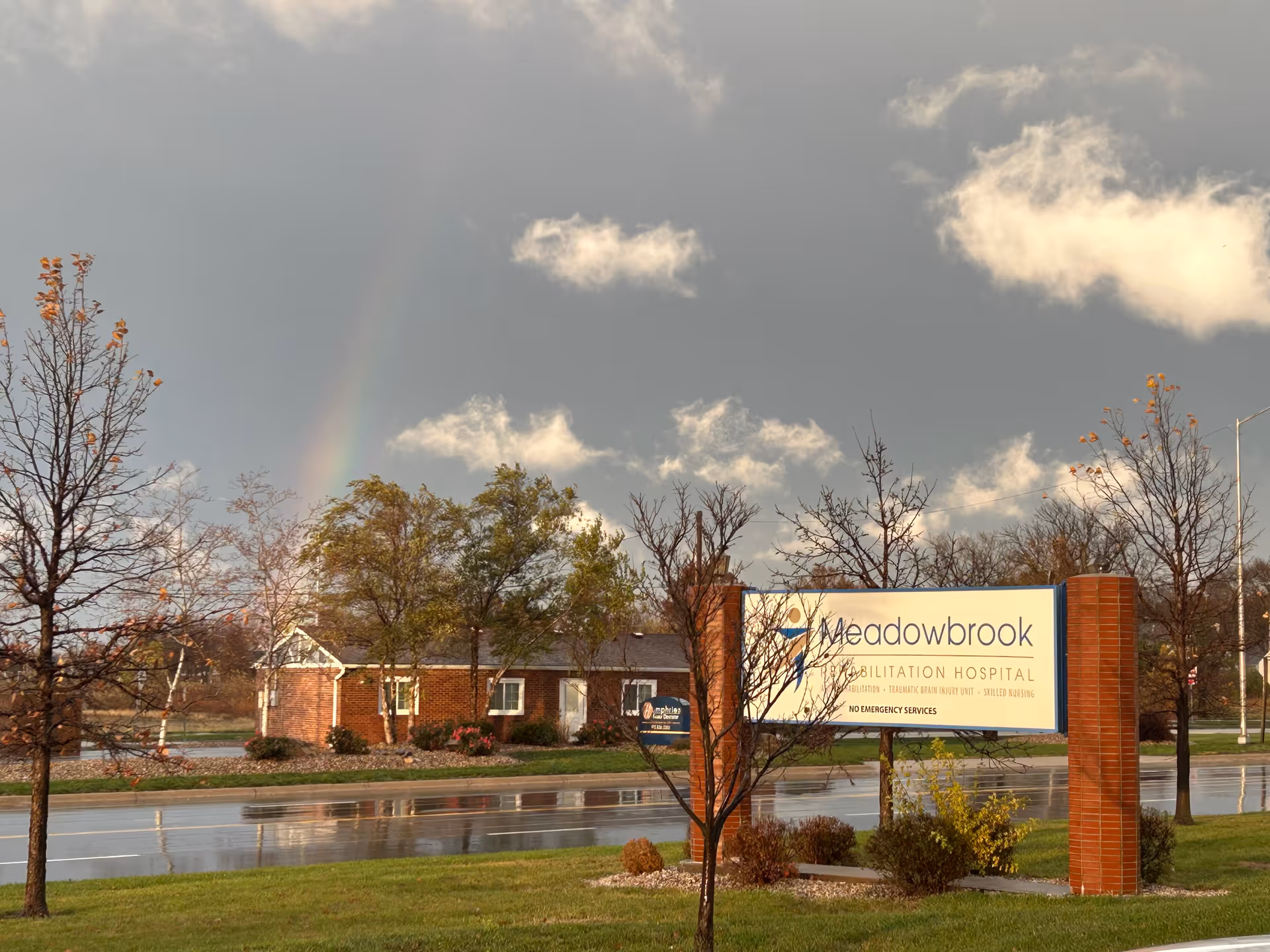 Exterior view of Meadowbrook Rehabilitation Hospital sign and brick entrance under rainbow sky