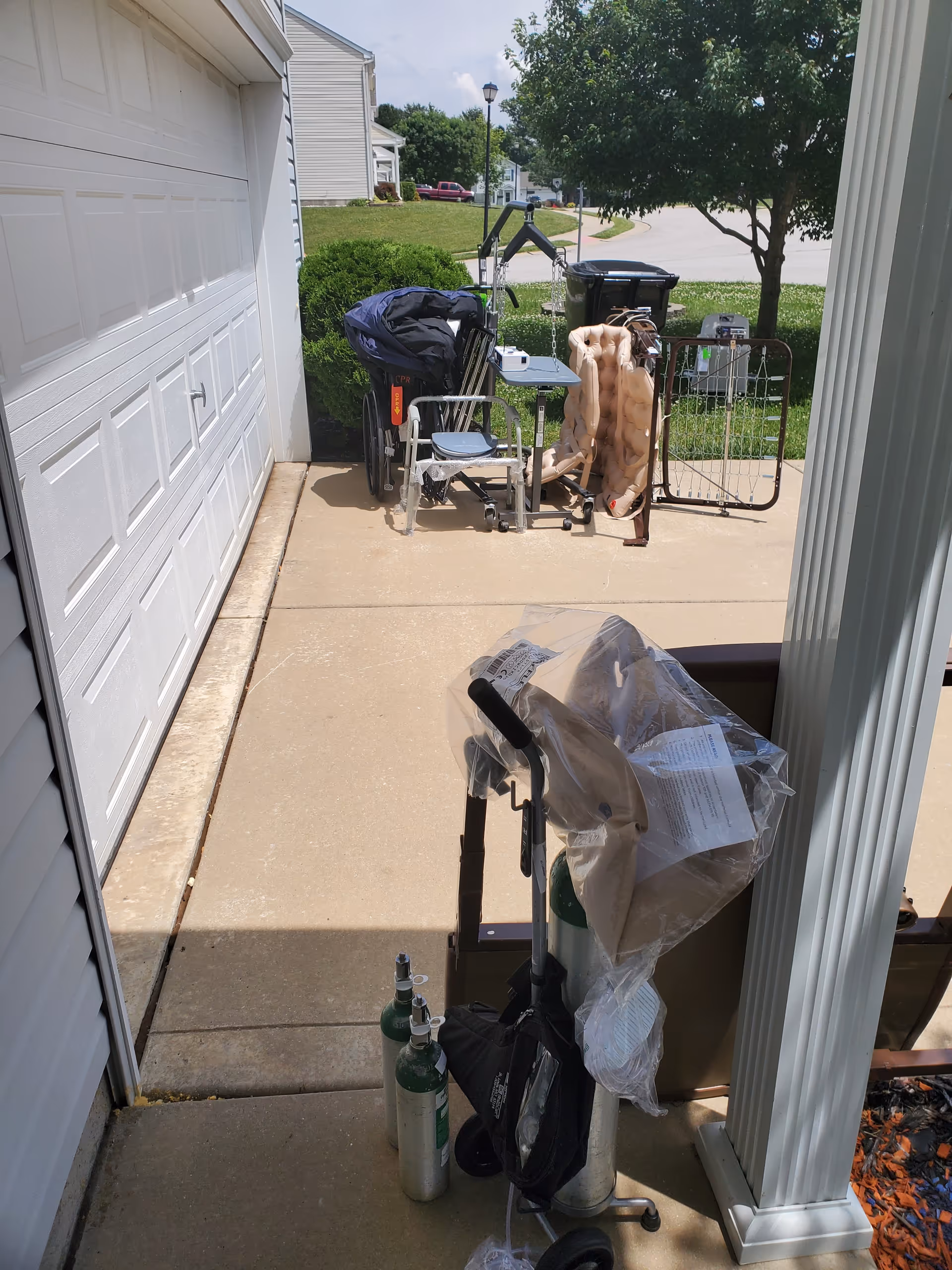 Outdoor driveway with mobility aids, oxygen tanks, and chairs near a garage.