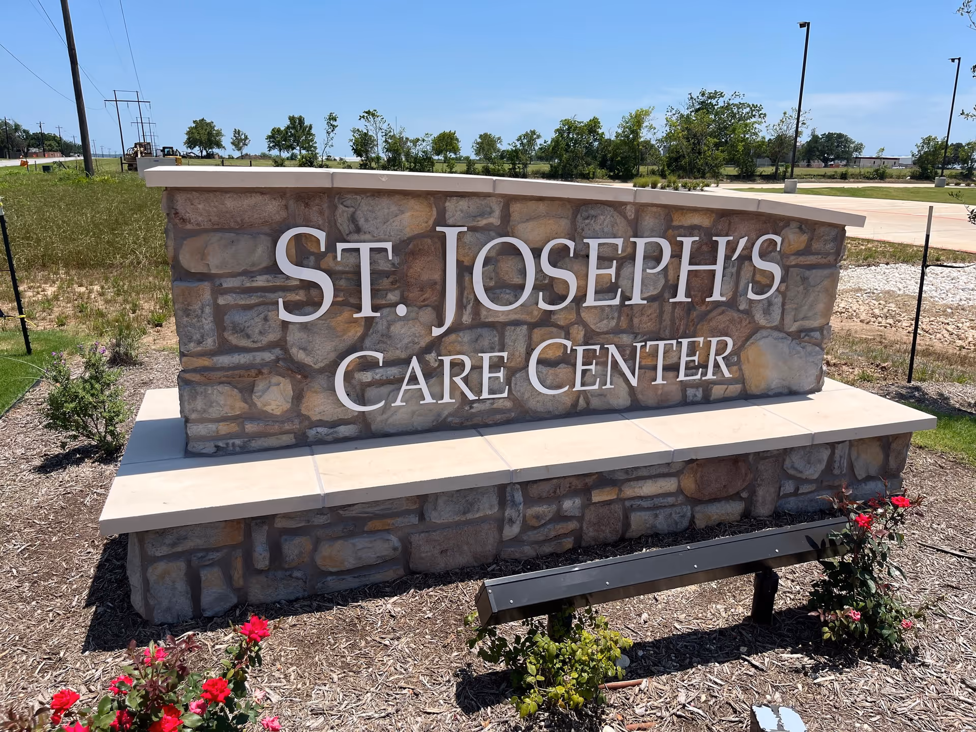 Stone sign reading St. Joseph's Care Center stands at an outdoor landscaped entrance.