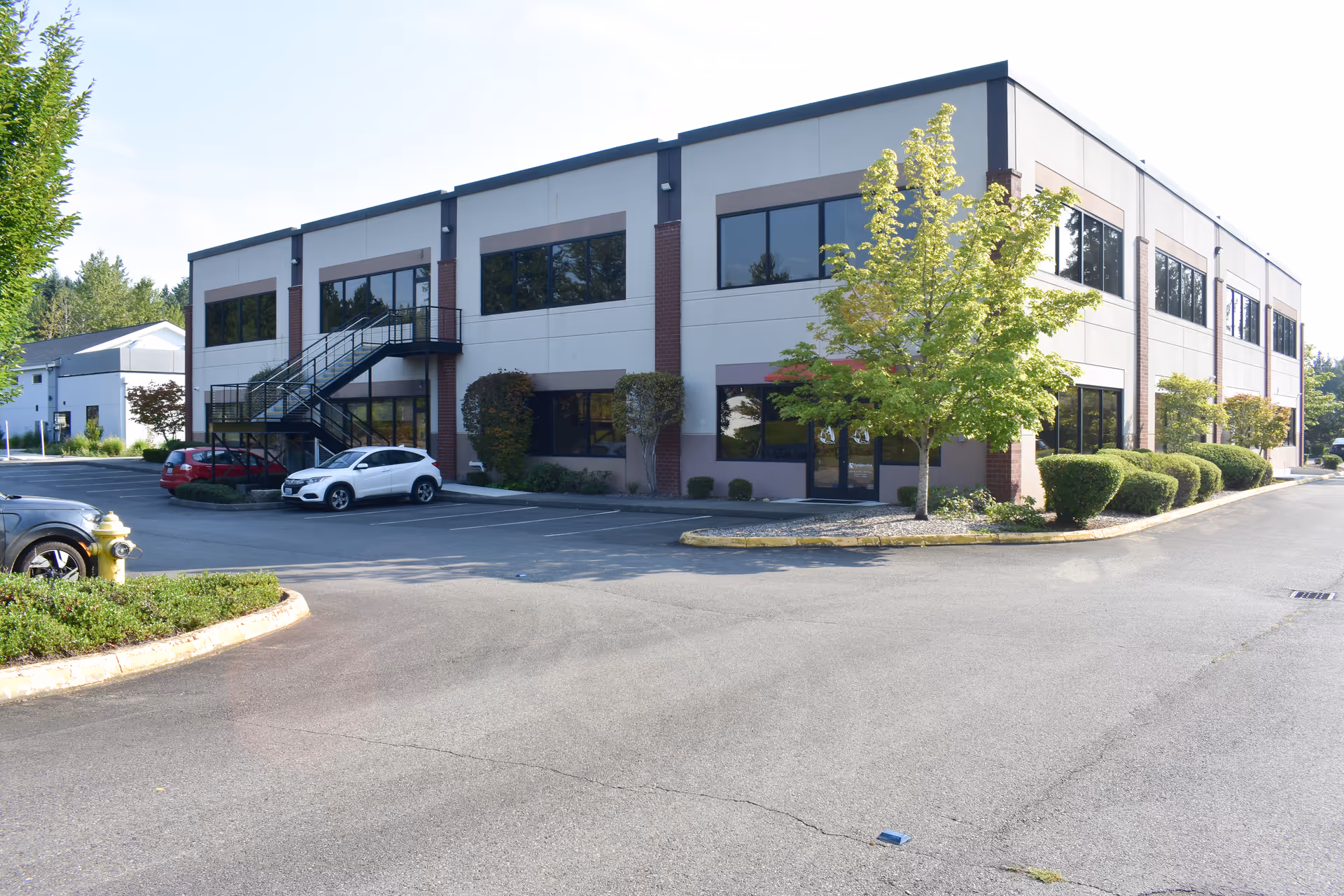 Two-story modern building with large windows, a parking lot, and well-kept landscaping.