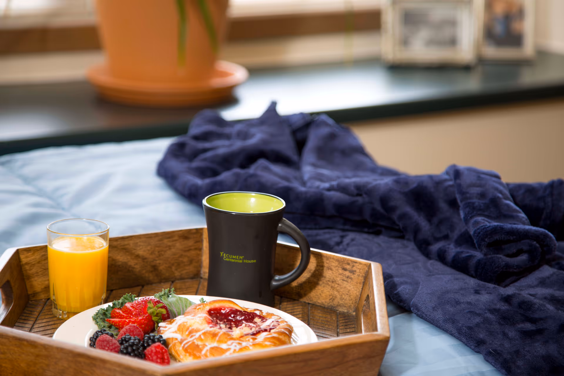 Breakfast tray with juice, a mug, and pastry on a bed in a cozy room.