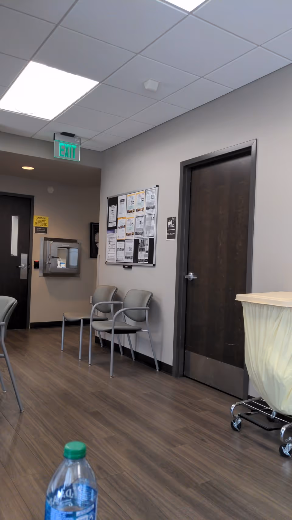 Interior waiting area with chairs, bulletin board, exit sign, and closed doors.
