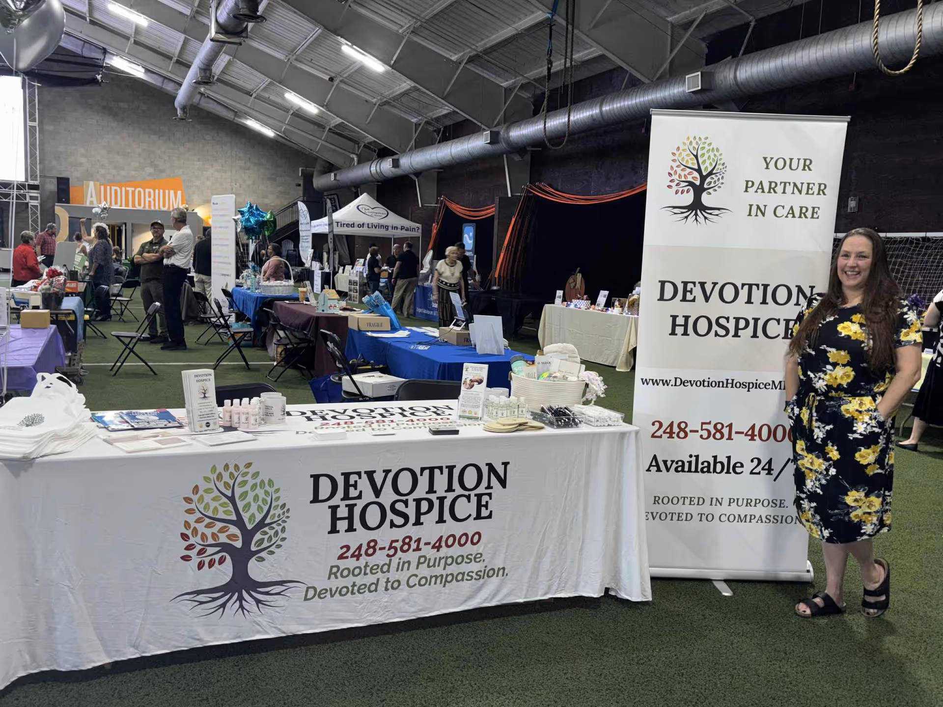 Indoor event with Devotion Hospice booth, banners, and staff at tables.
