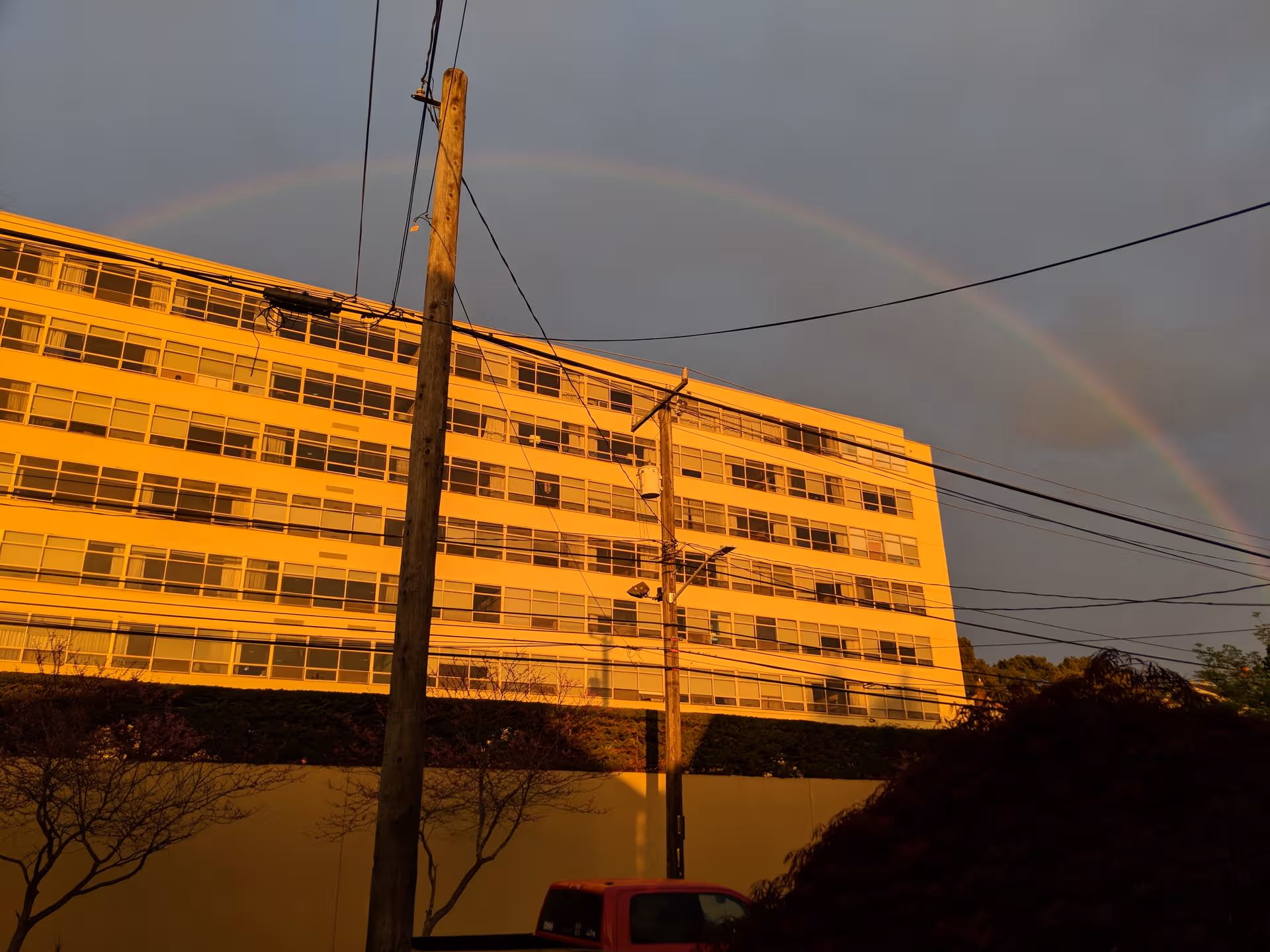 Sunlit exterior of a multi-story senior living building with a rainbow overhead.