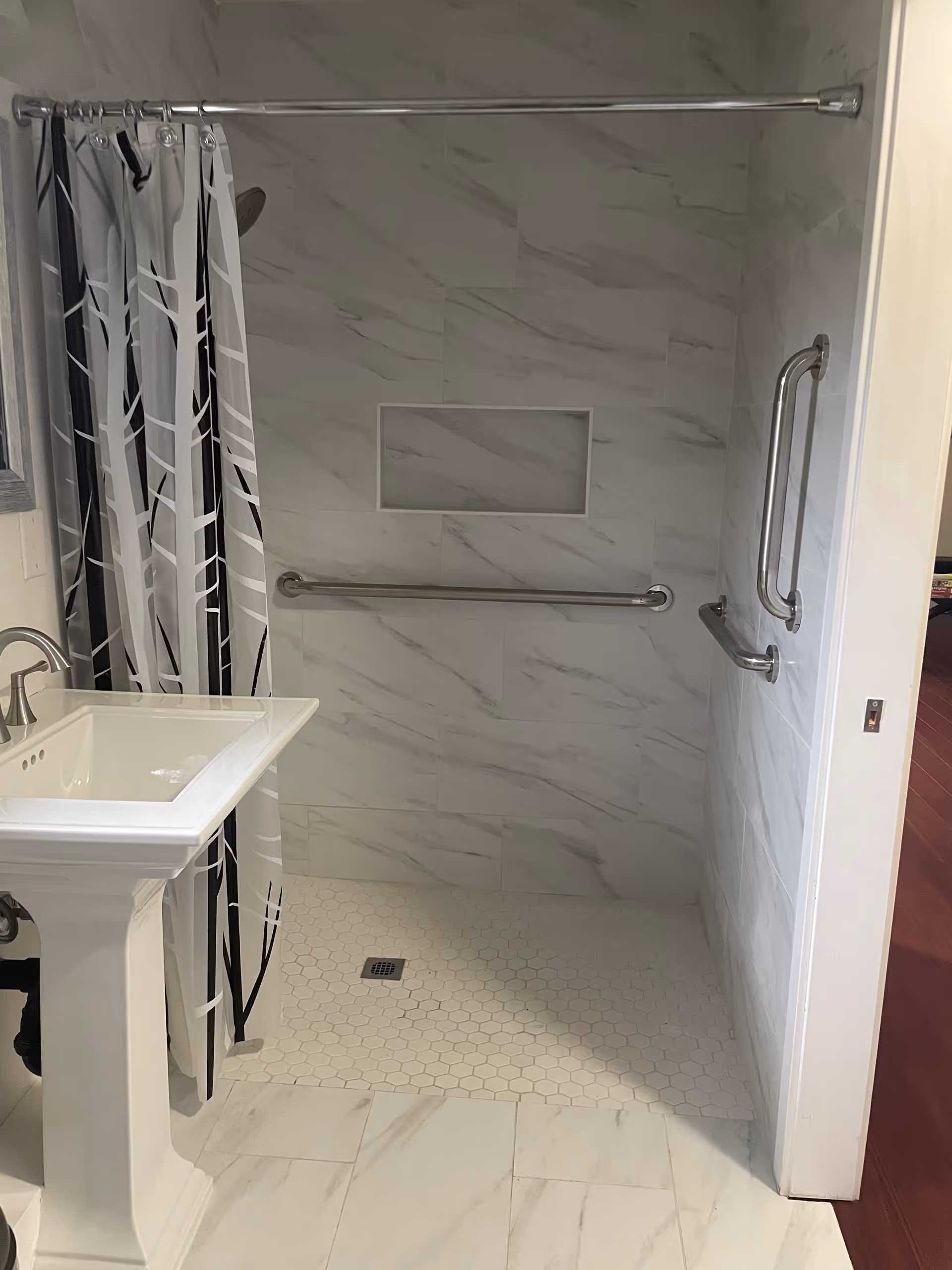 Wheelchair-accessible bathroom with marble walls, shower curtain, grab bars, a shower niche, and a pedestal sink.