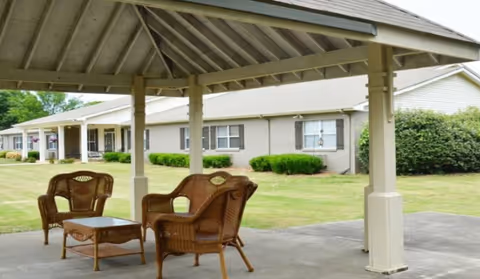 Outdoor seating area with wicker chairs under a pavilion in front of a senior living facility.