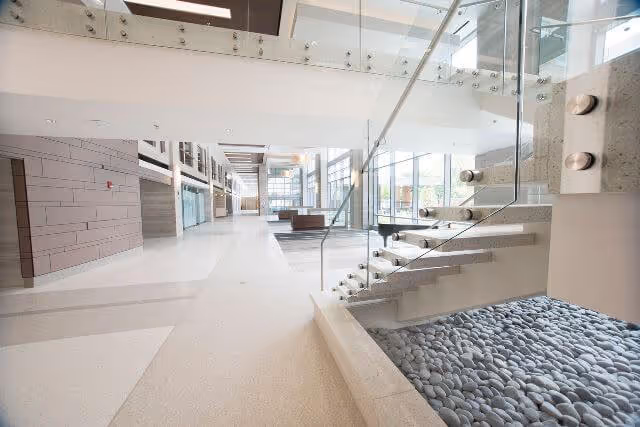 Bright modern interior atrium with a glass staircase, pebble feature, and seating area.