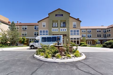 Front view of The Seasons of Reno senior living campus with circular driveway fountain and bus.
