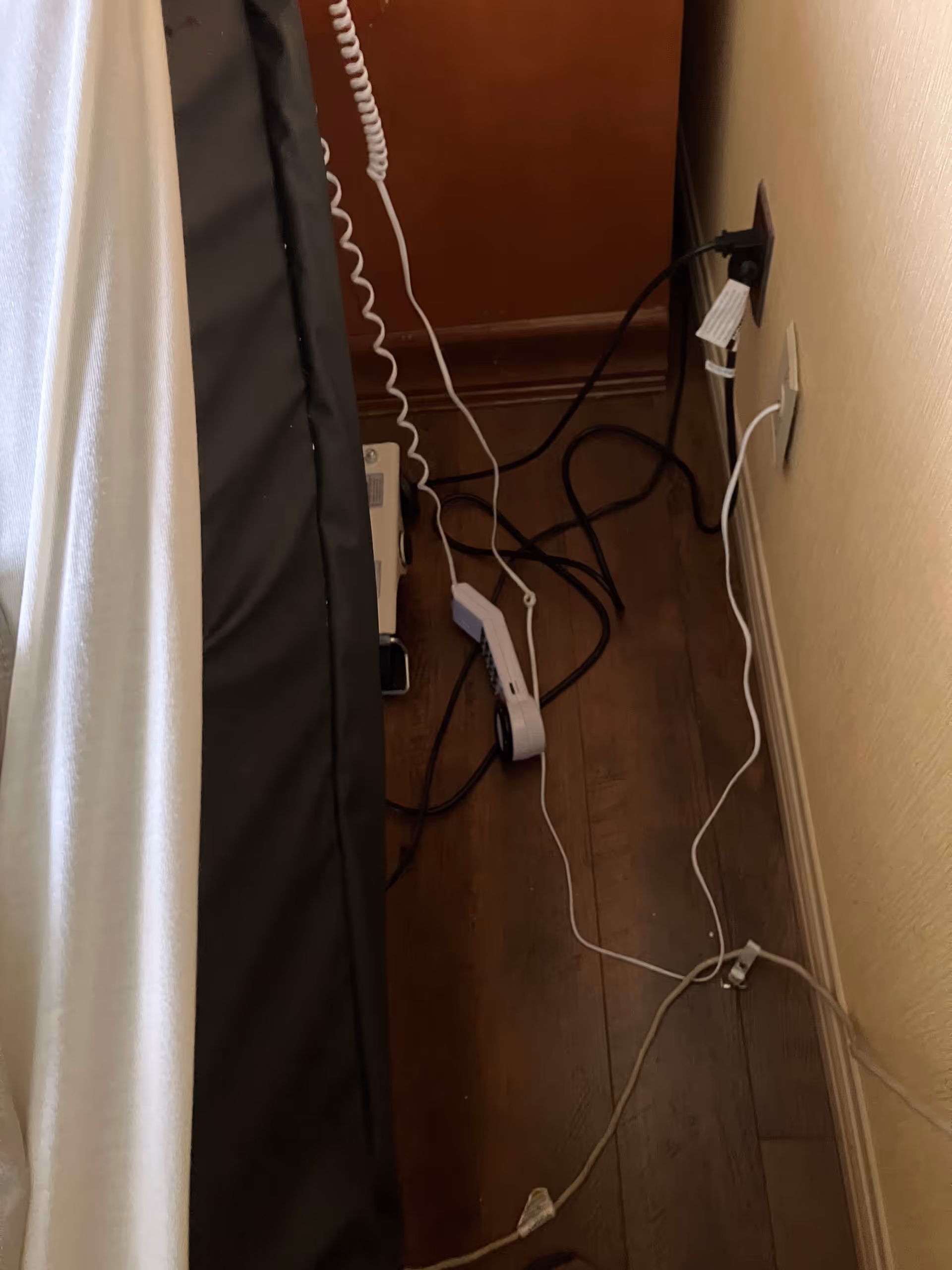 Corner of a room with tangled cords and power strips by a bed.
