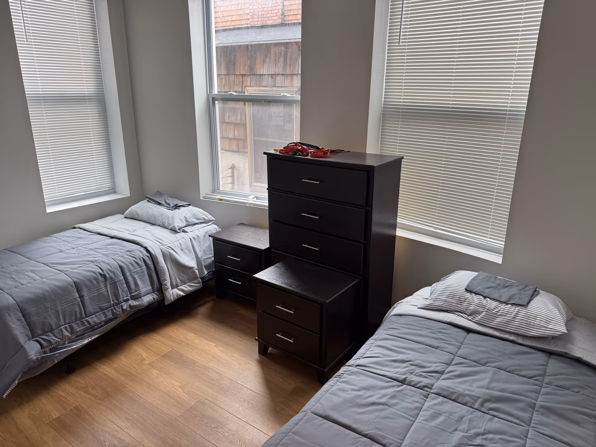Two twin beds with gray bedding flank a tall dresser in a bright bedroom.