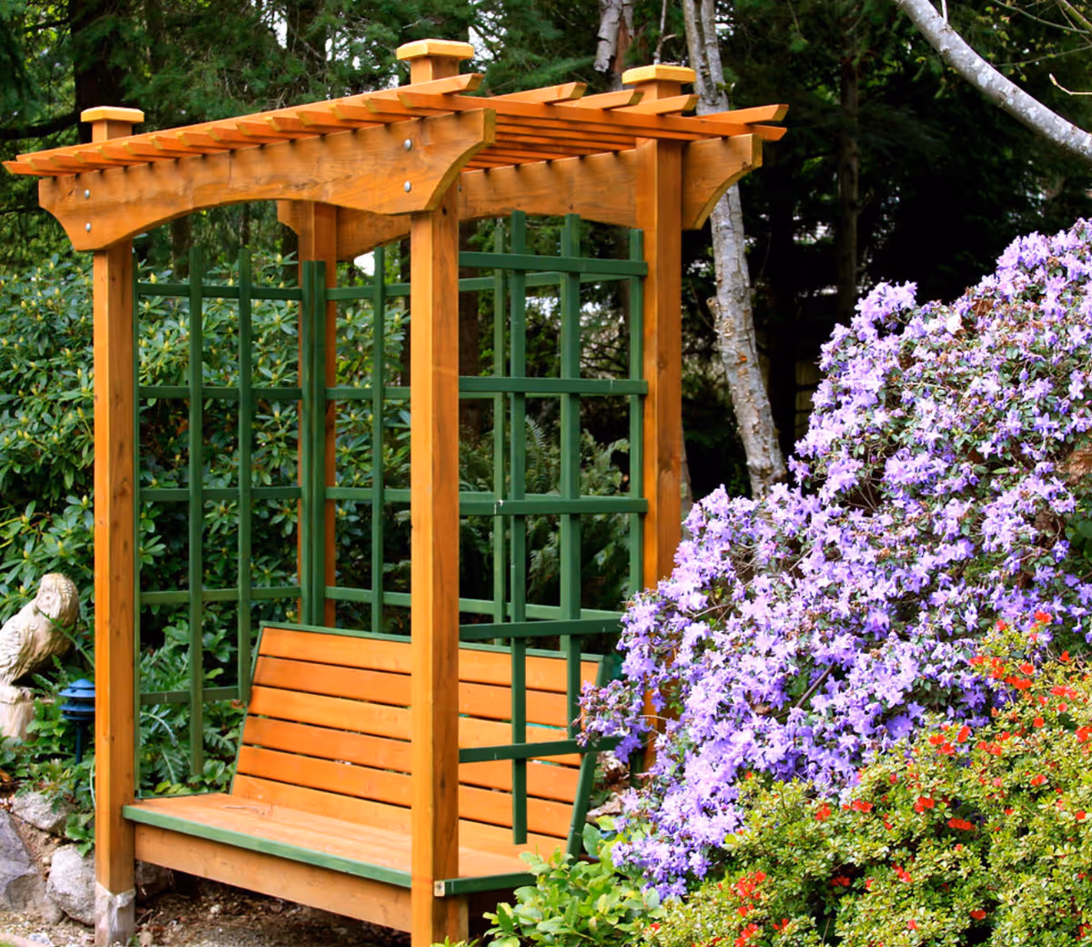 Outdoor wooden garden arbor with bench surrounded by purple flowers.