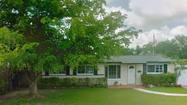 Single-story facility front with a green lawn, trees, and a white entrance door.