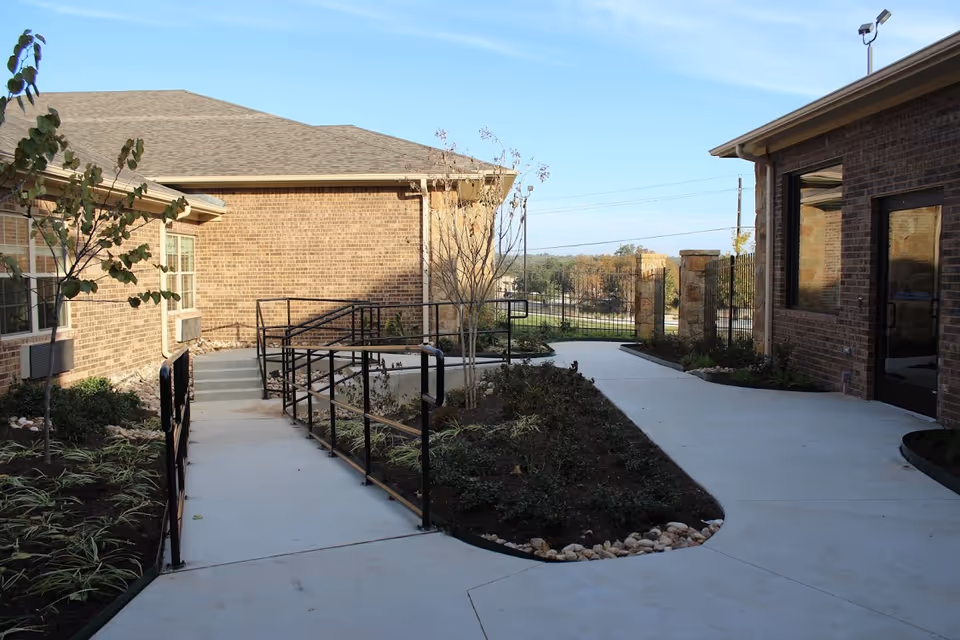 Brick senior living campus courtyard with paved walkway, ramps, and landscaped beds.