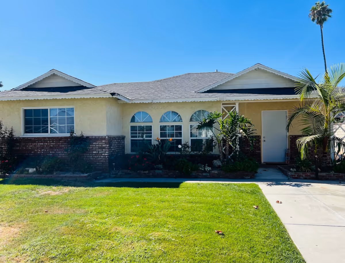 Single-story beige building with arched windows, front yard, and a driveway leading to a door.