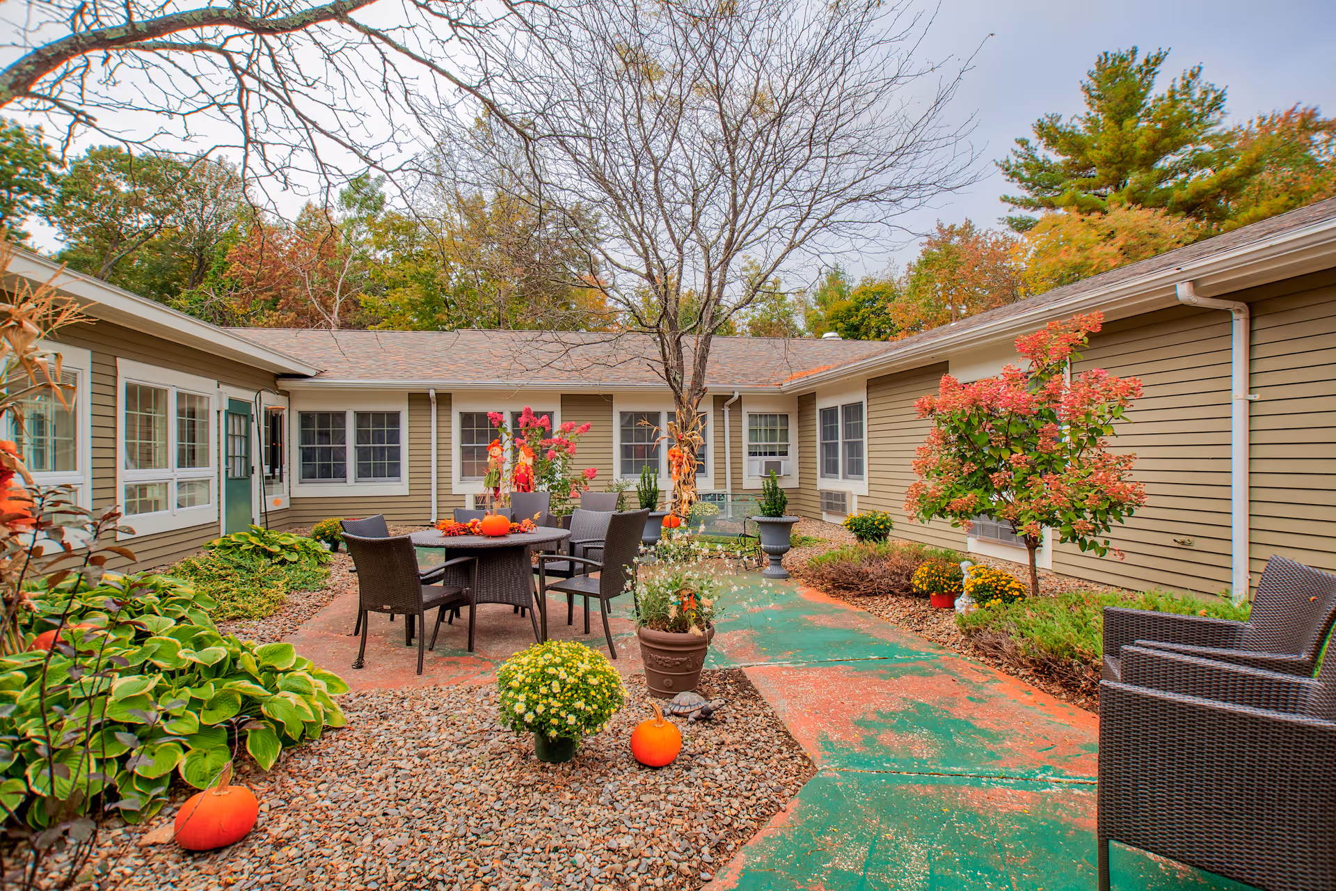 An outdoor courtyard with tables, chairs, pumpkins, and potted plants between beige housing units.