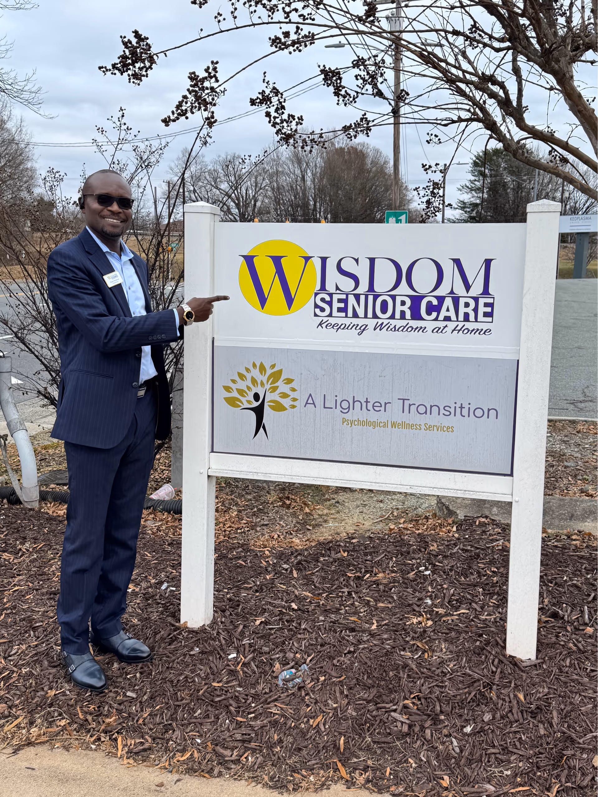 Man in suit points at Wisdom Senior Care Burlington sign outside facility