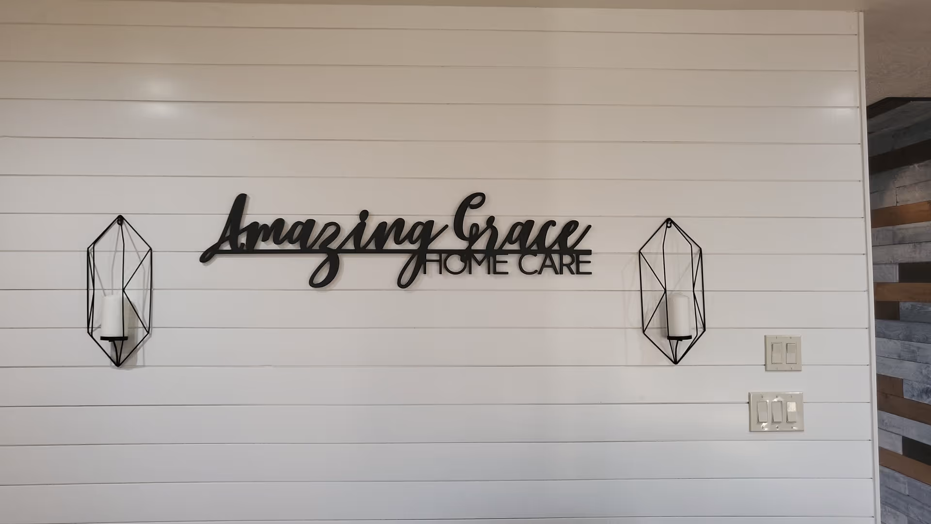 White paneled interior wall with Amazing Grace Home Care sign and geometric wall sconces.