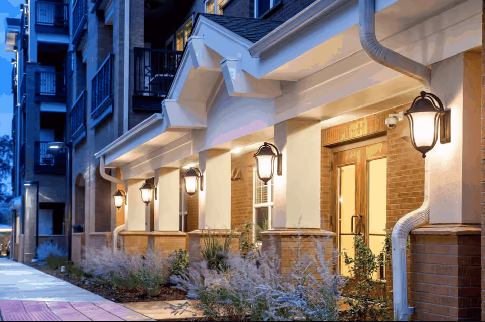 Exterior view of Clermont Park Assisted Living building with lit entry doors along the walkway.
