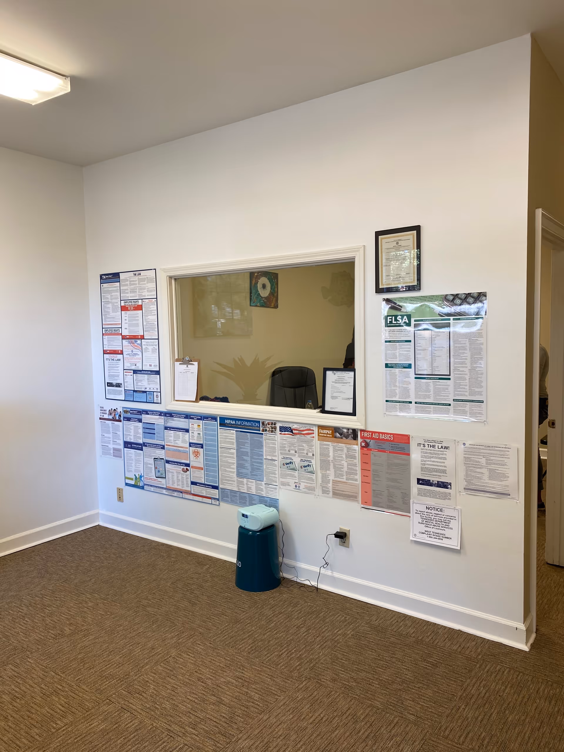 Interior wall with posted notices and a windowed reception area.
