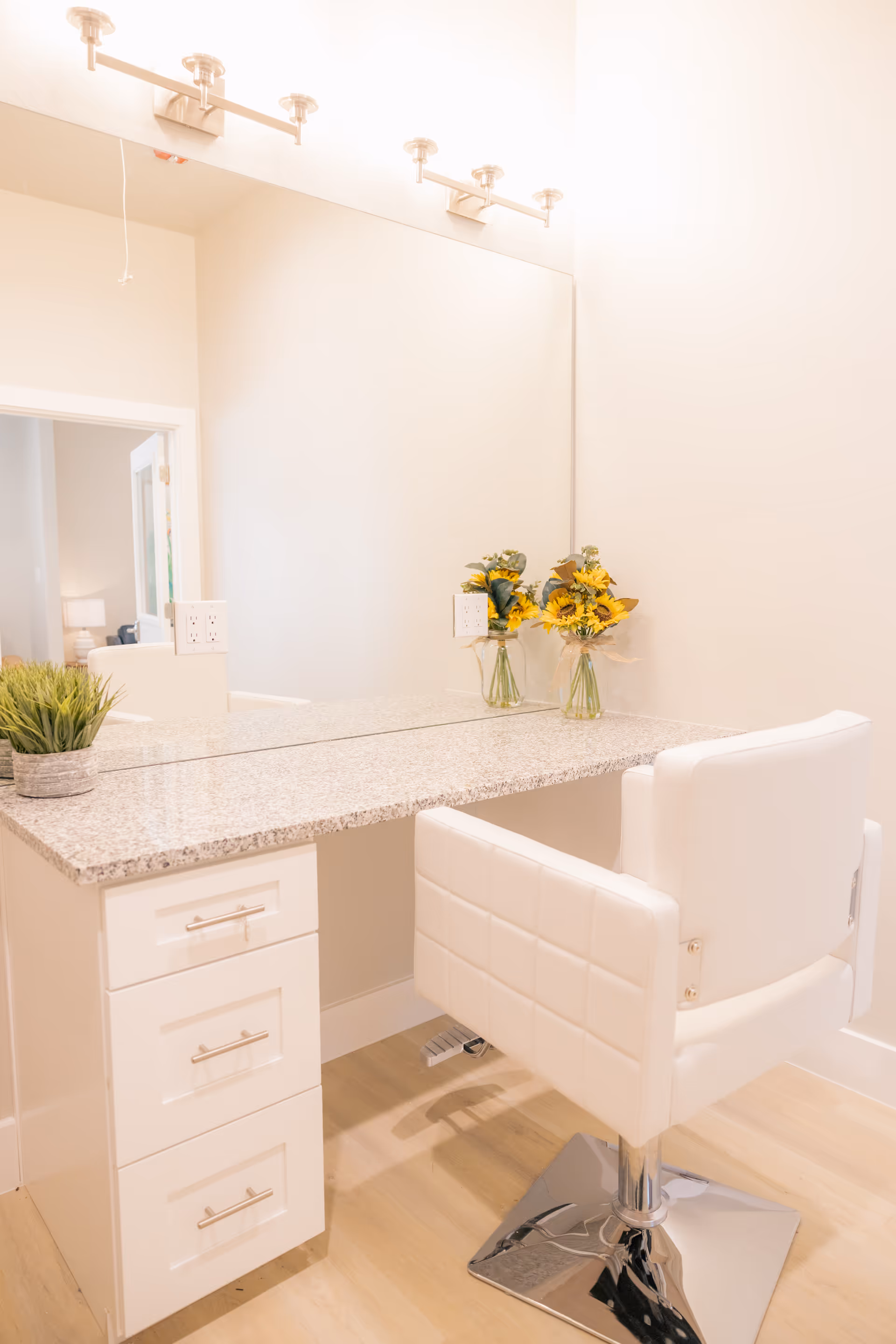 White bathroom vanity with granite countertop, large mirror, and a white cushioned chair.