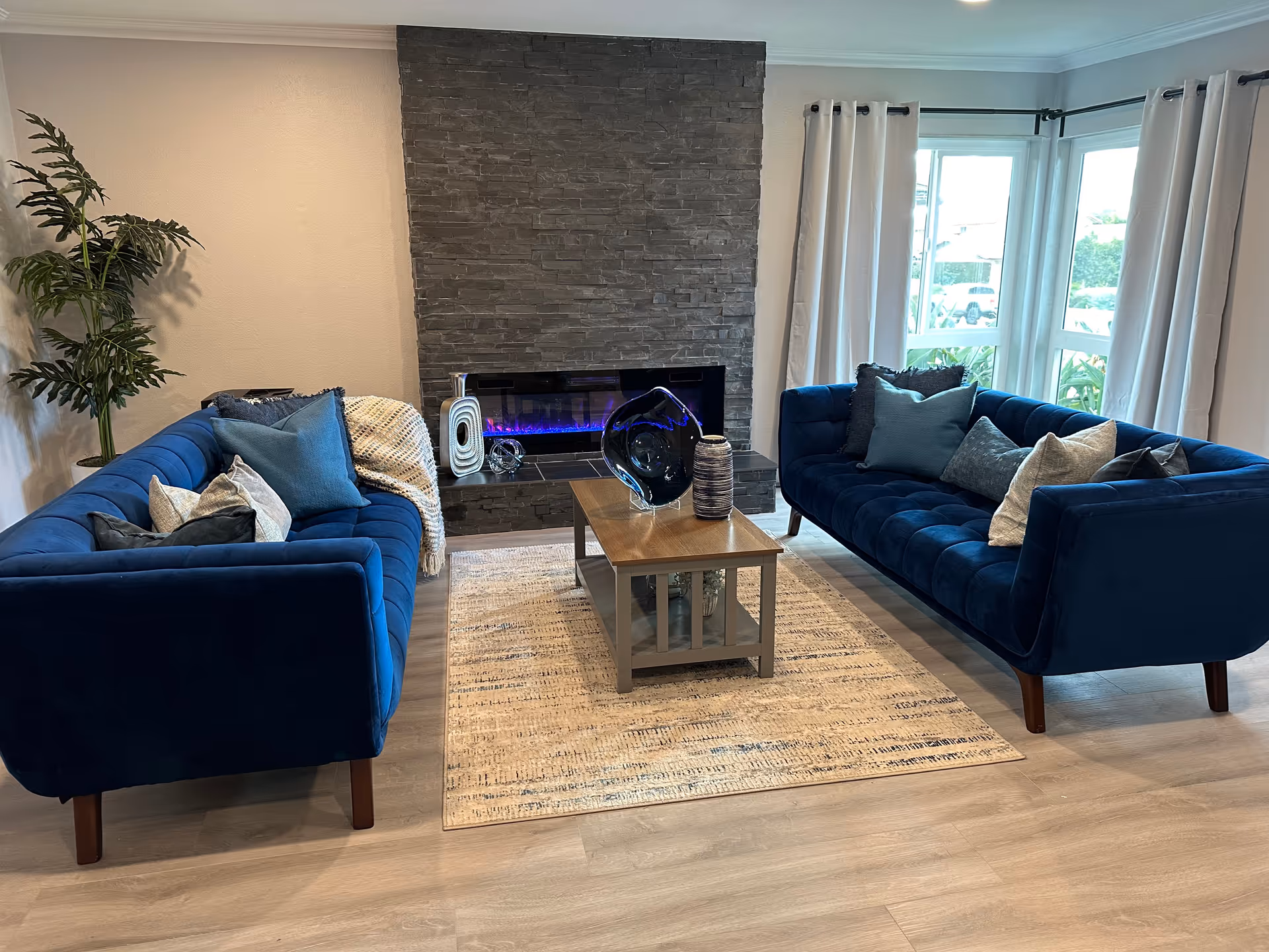 Two blue velvet sofas face a coffee table with a stone fireplace in a living room.