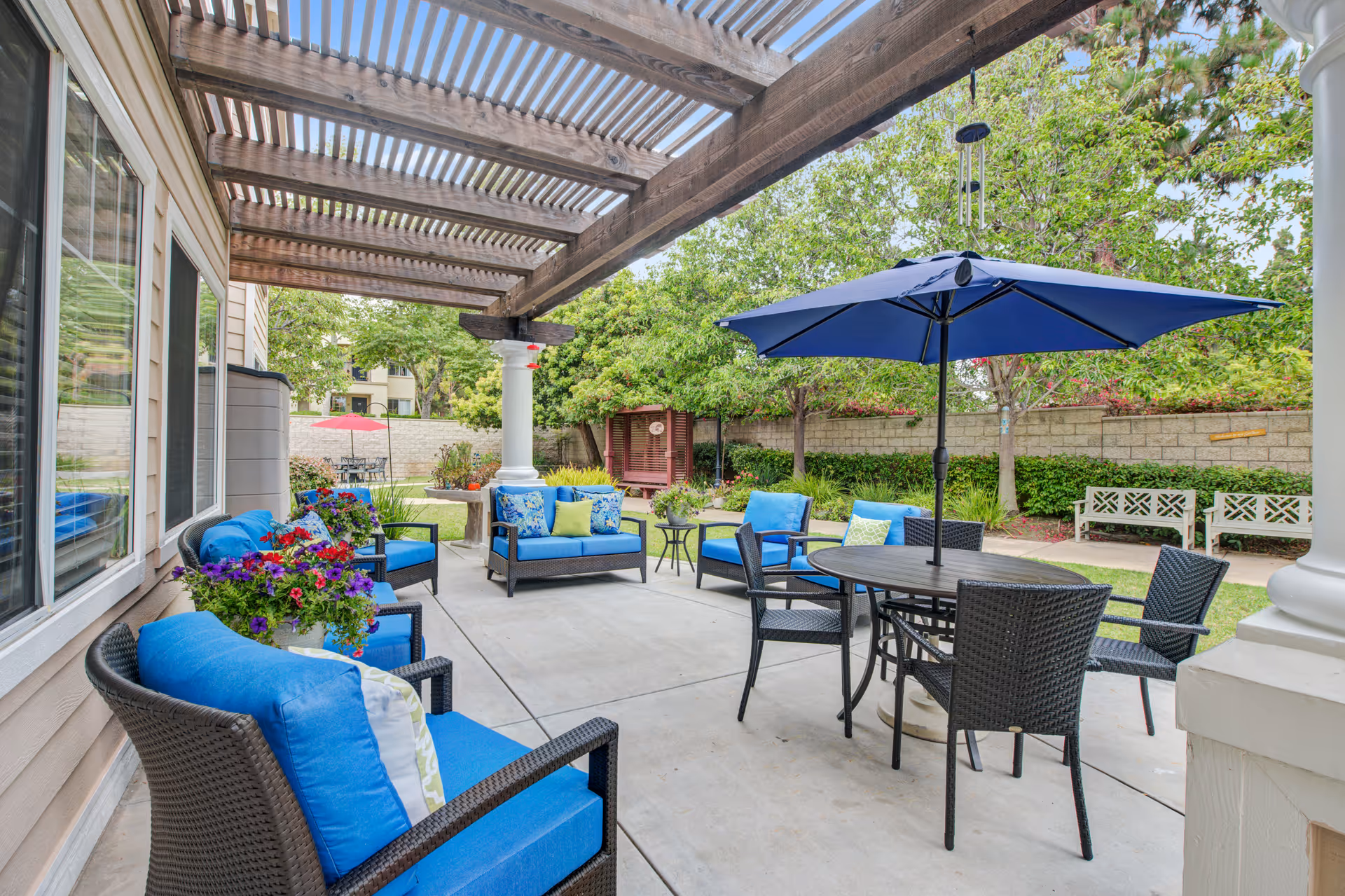 Outdoor patio under a pergola with blue-cushioned seating and a large umbrella.