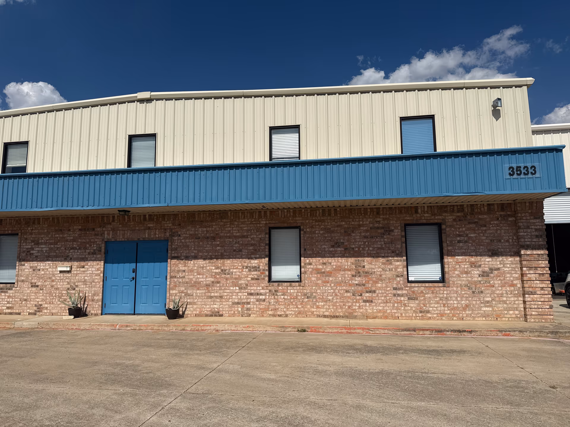 Two-story brick building with beige upper level, blue accents, and closed windows.