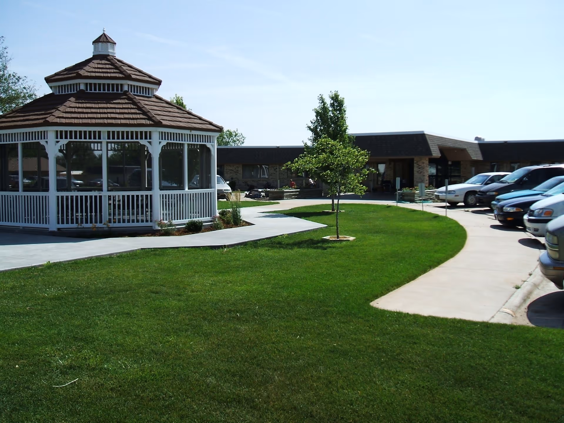 Exterior of Bethel Home Inc.: white gazebo, green lawn, single-story building, and parked cars.