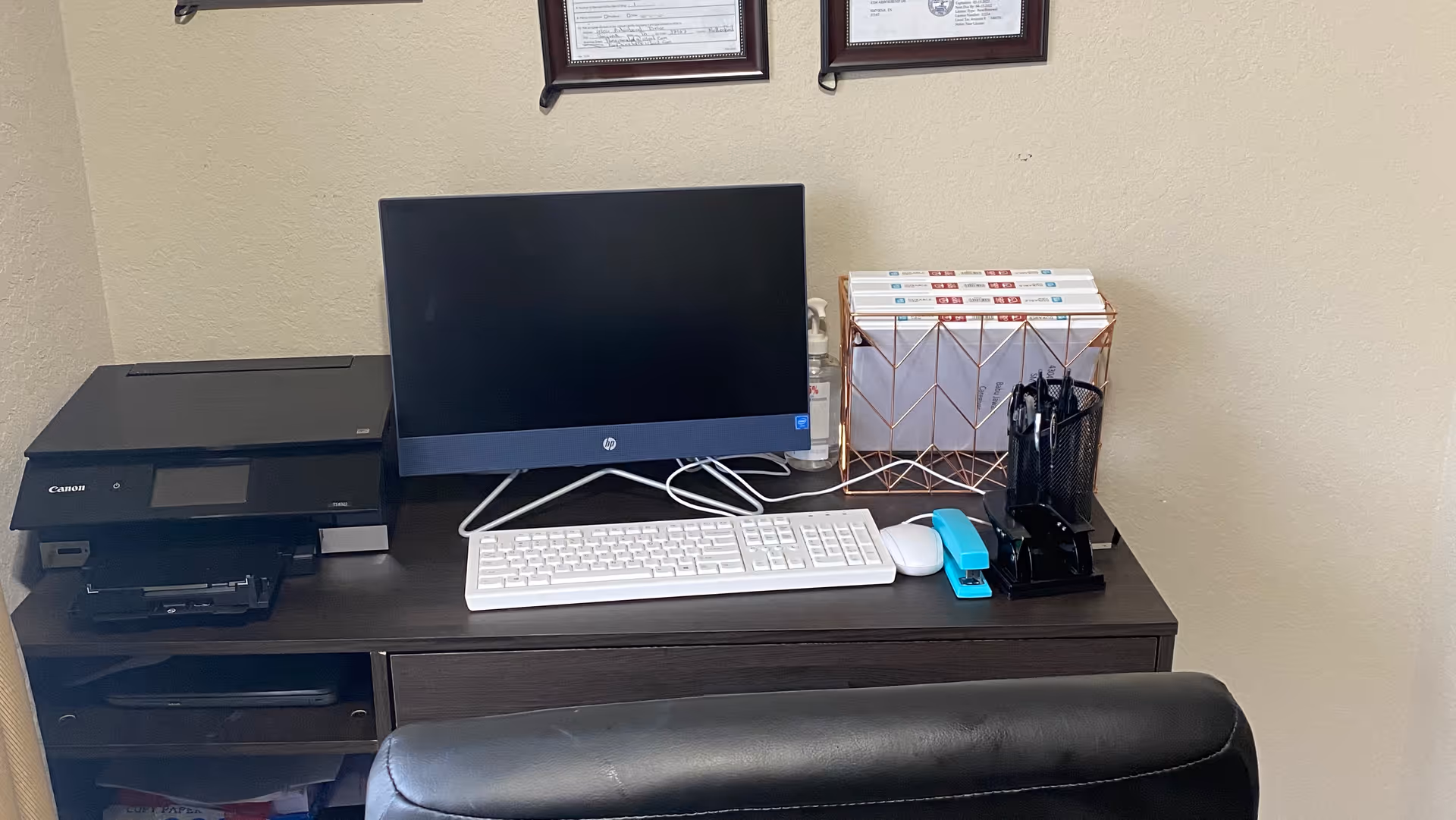 A dark desk with computer monitor, printer, keyboard, and office supplies.