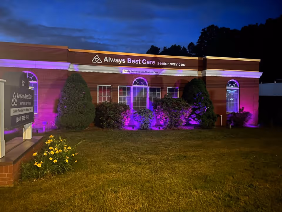 Nighttime exterior of Always Best Care Senior Services building illuminated with purple lighting.