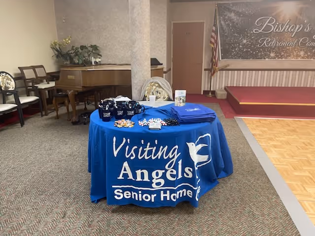Indoor lobby with a blue Visiting Angels table and stage area.