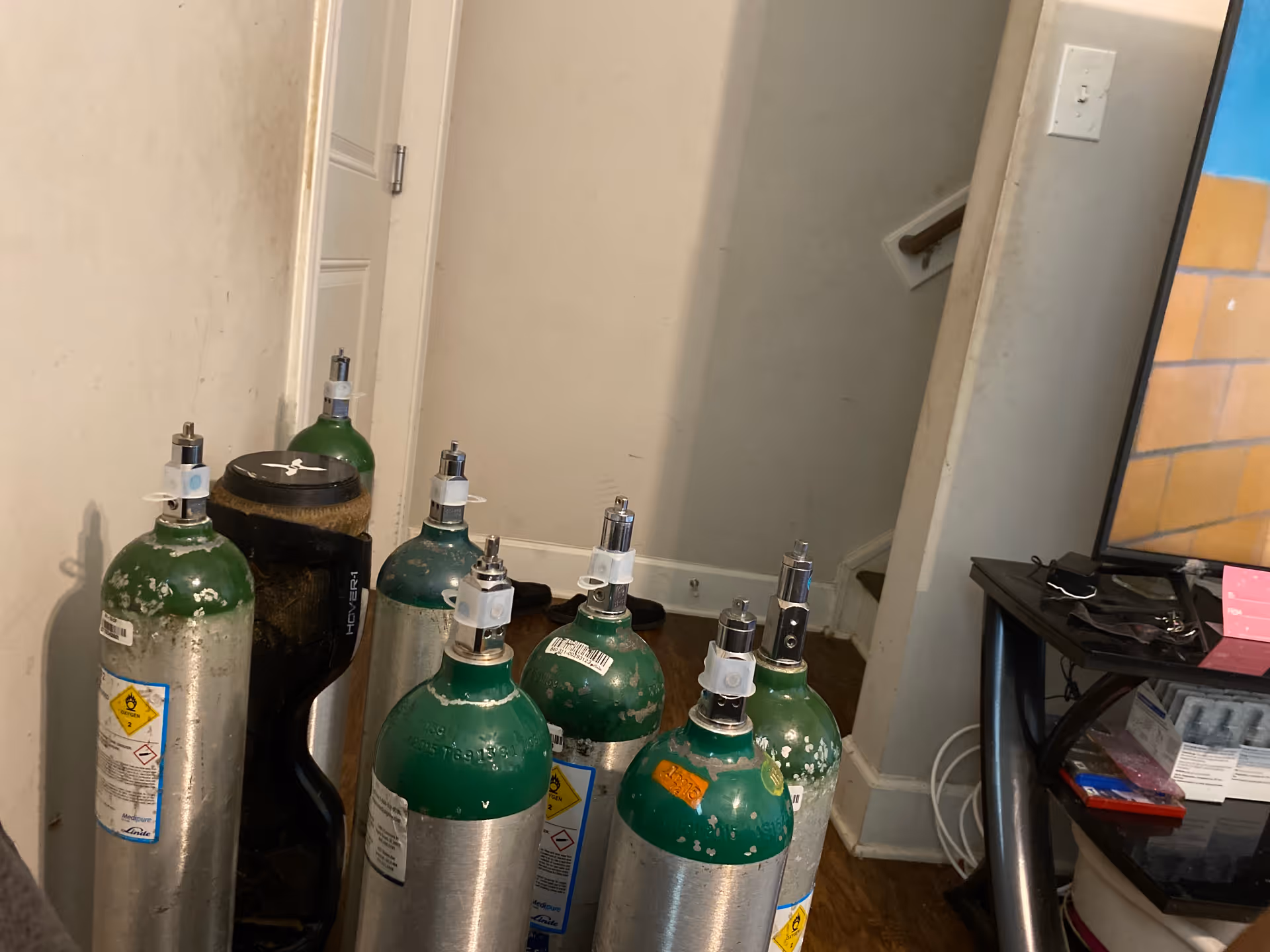 Interior room featuring multiple green oxygen tanks lined up next to a mirror and TV stand.
