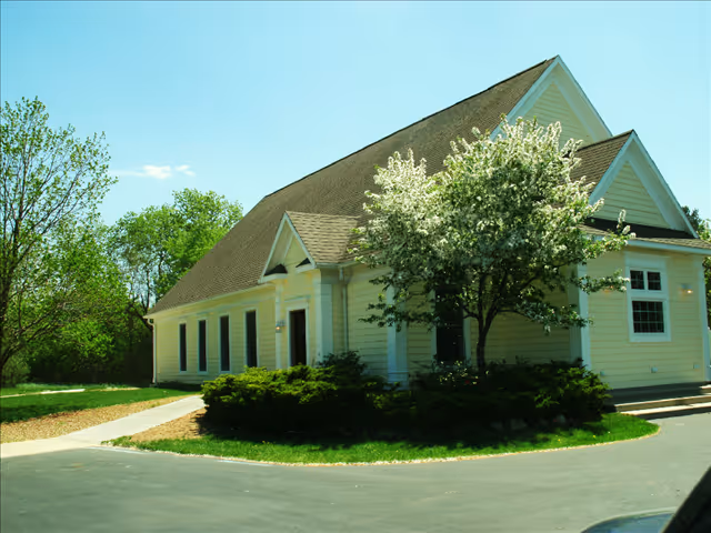 A single-story yellow building with a sloped roof surrounded by greenery.
