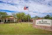A single-story facility exterior with a flagpole, lawn, and Opp Health and Rehabilitation sign.