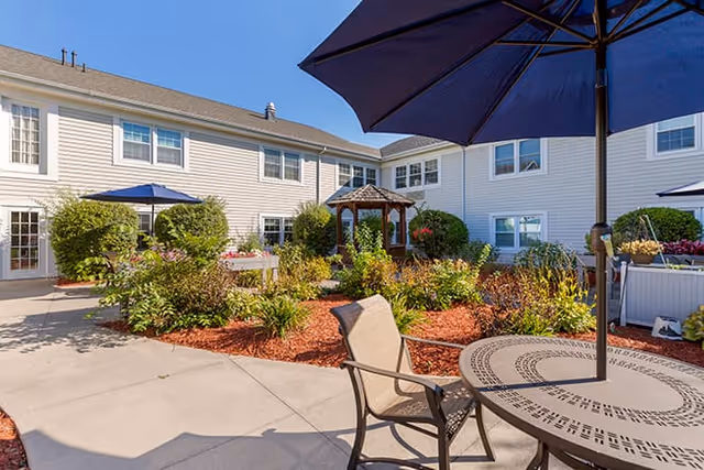 Outdoor courtyard with seating, umbrellas, and garden landscaping at Brookdale Northville.
