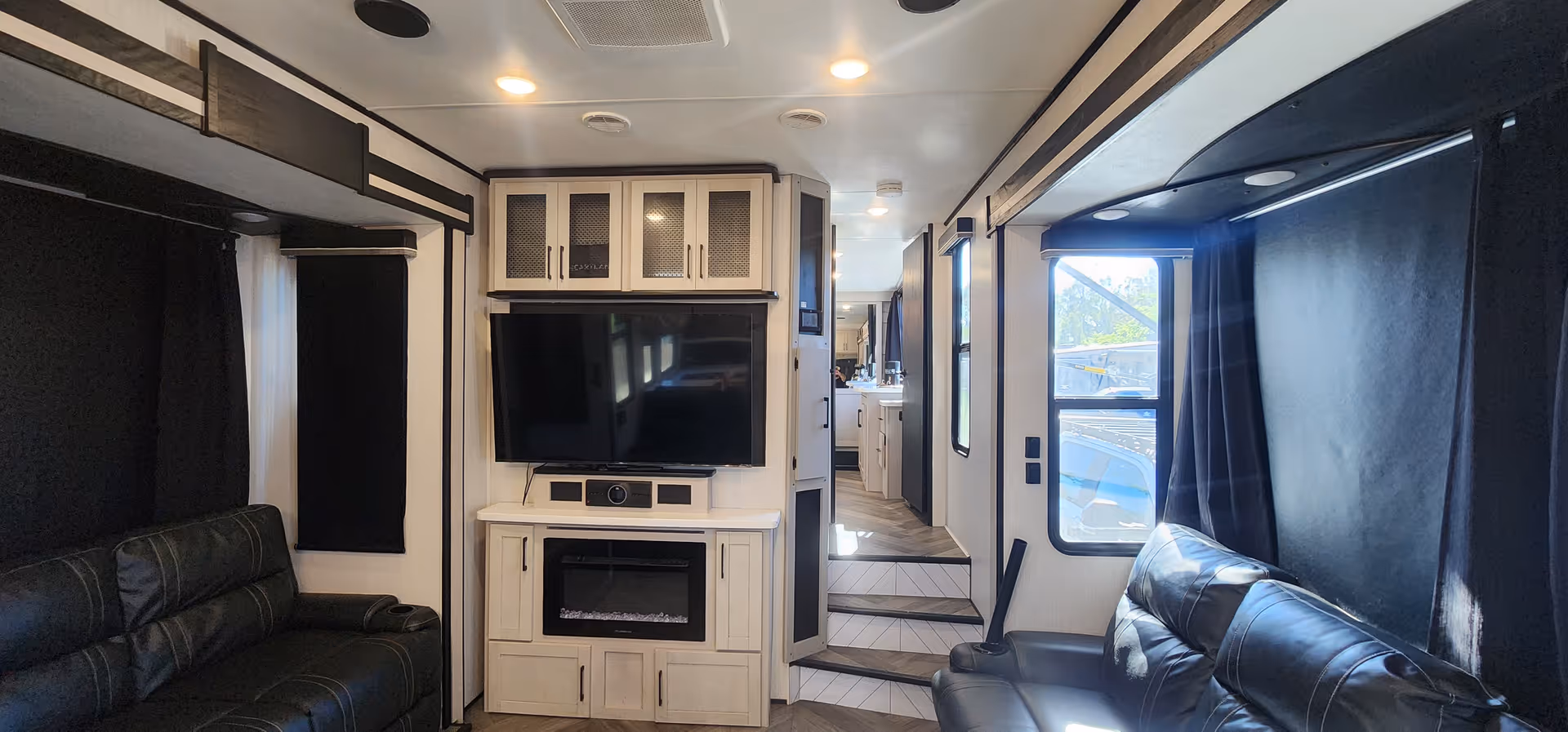 Interior living area with leather couches, a wall-mounted TV, cabinetry, and a fireplace.
