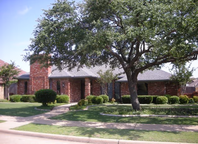 Front view of a brick senior living center with landscaping and a large tree.
