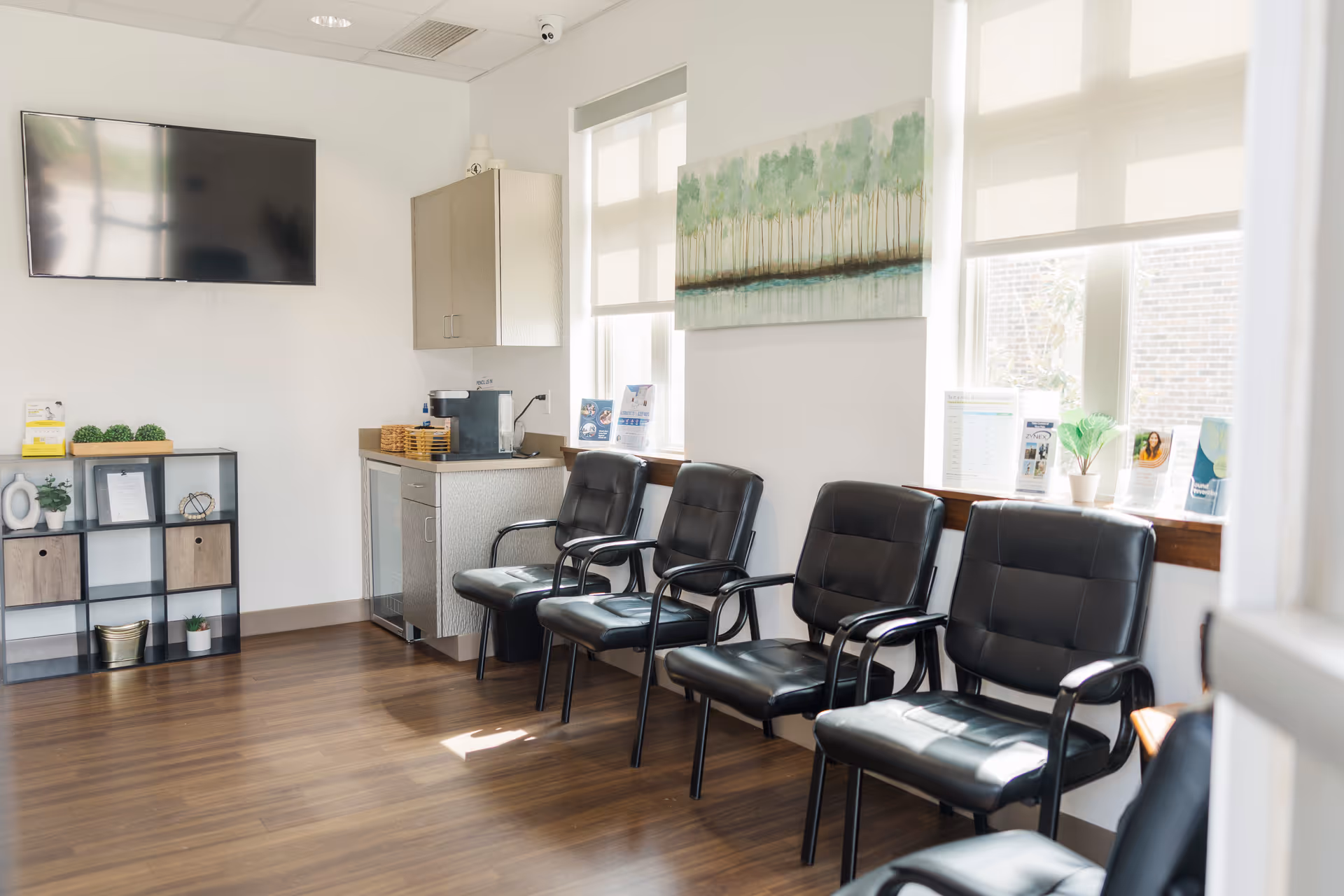 Bright interior lounge with black chairs, a coffee station, and a wall-mounted TV.