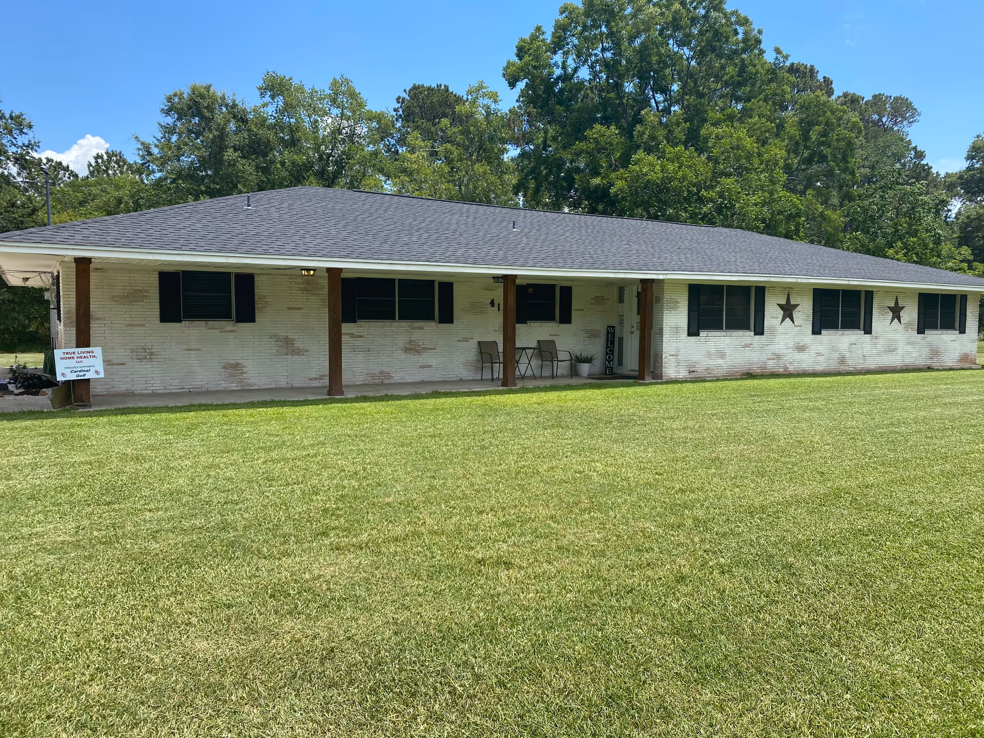 Long, single-story white brick facility with a shaded front porch and expansive green lawn.
