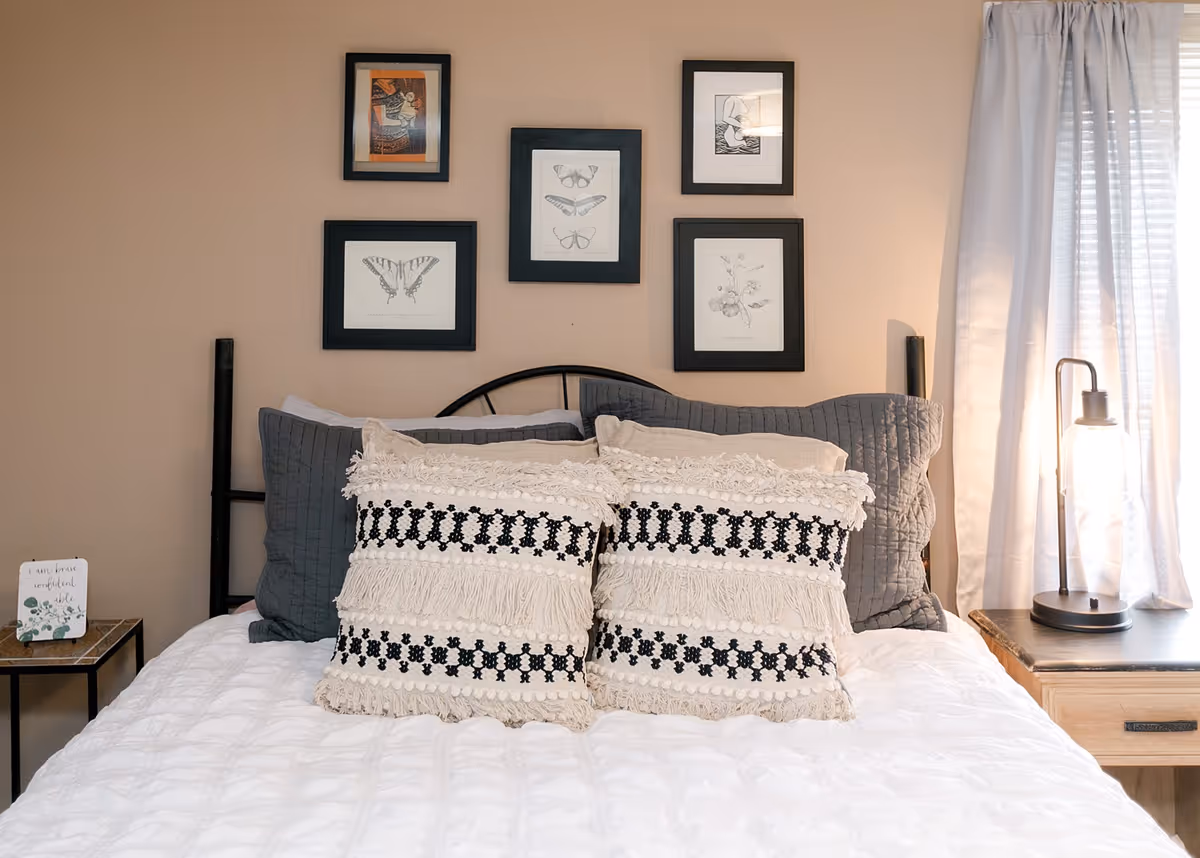 A neatly made bedroom with decorative pillows, nightstands, and framed wall art.