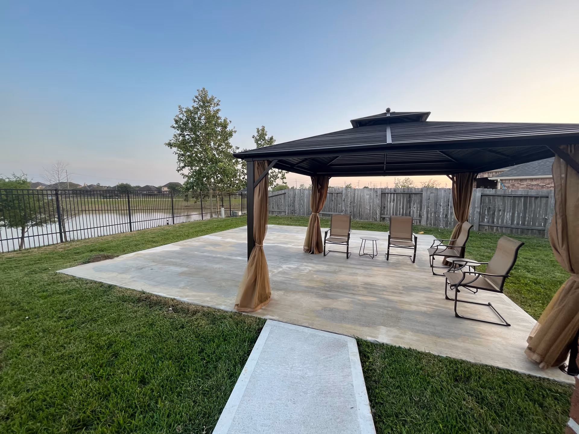 Outdoor gazebo with curtained canopy and multiple lounge chairs on a concrete patio.