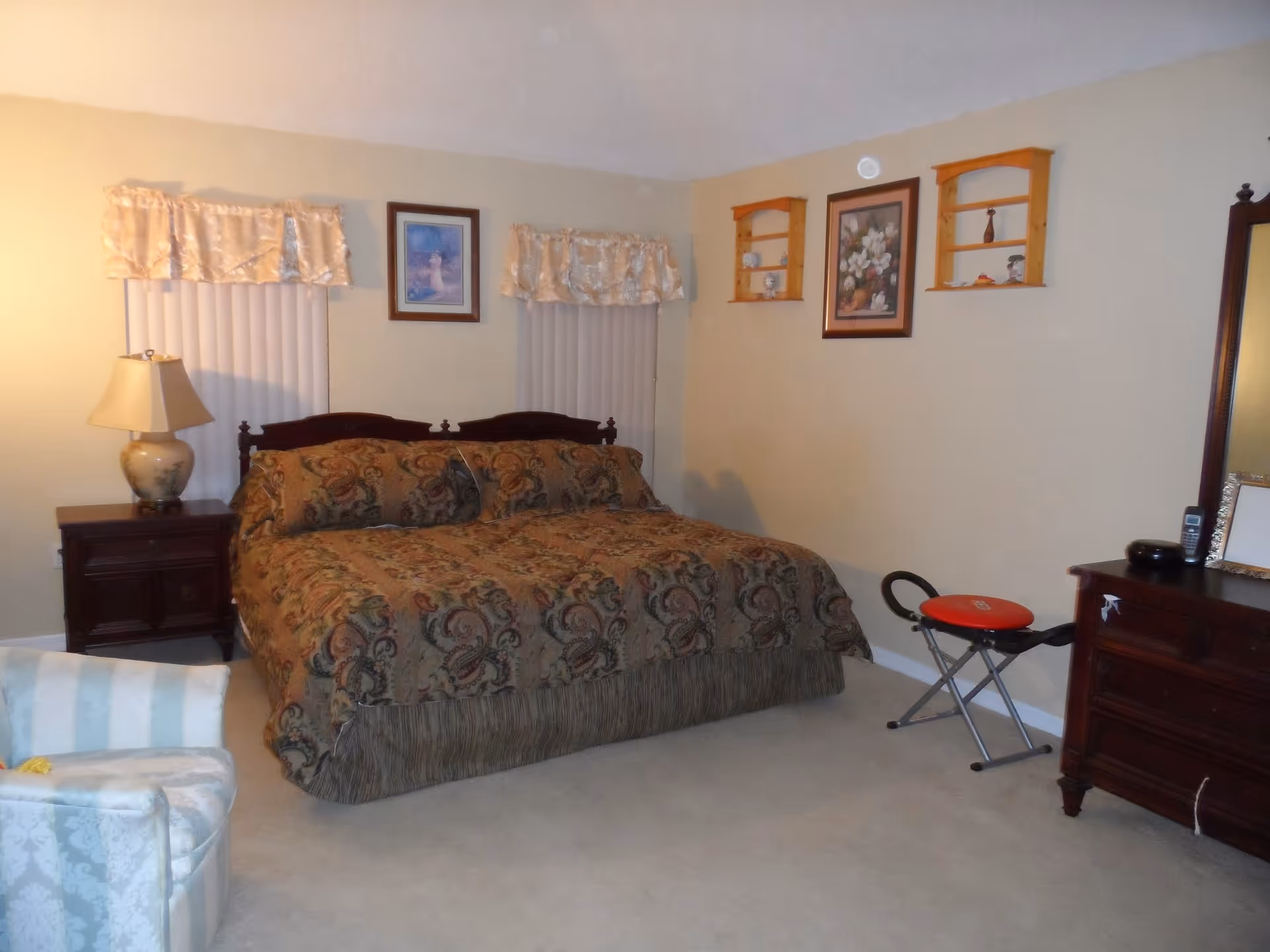 A cozy, furnished bedroom with a large bed, dresser, lamp, and seating.