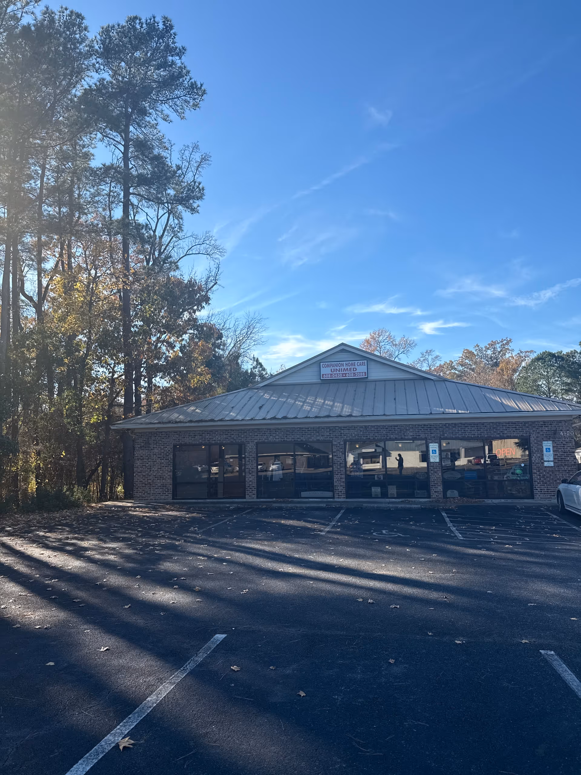 Front view of a brick senior care facility with large windows, sign, and adjacent parking.