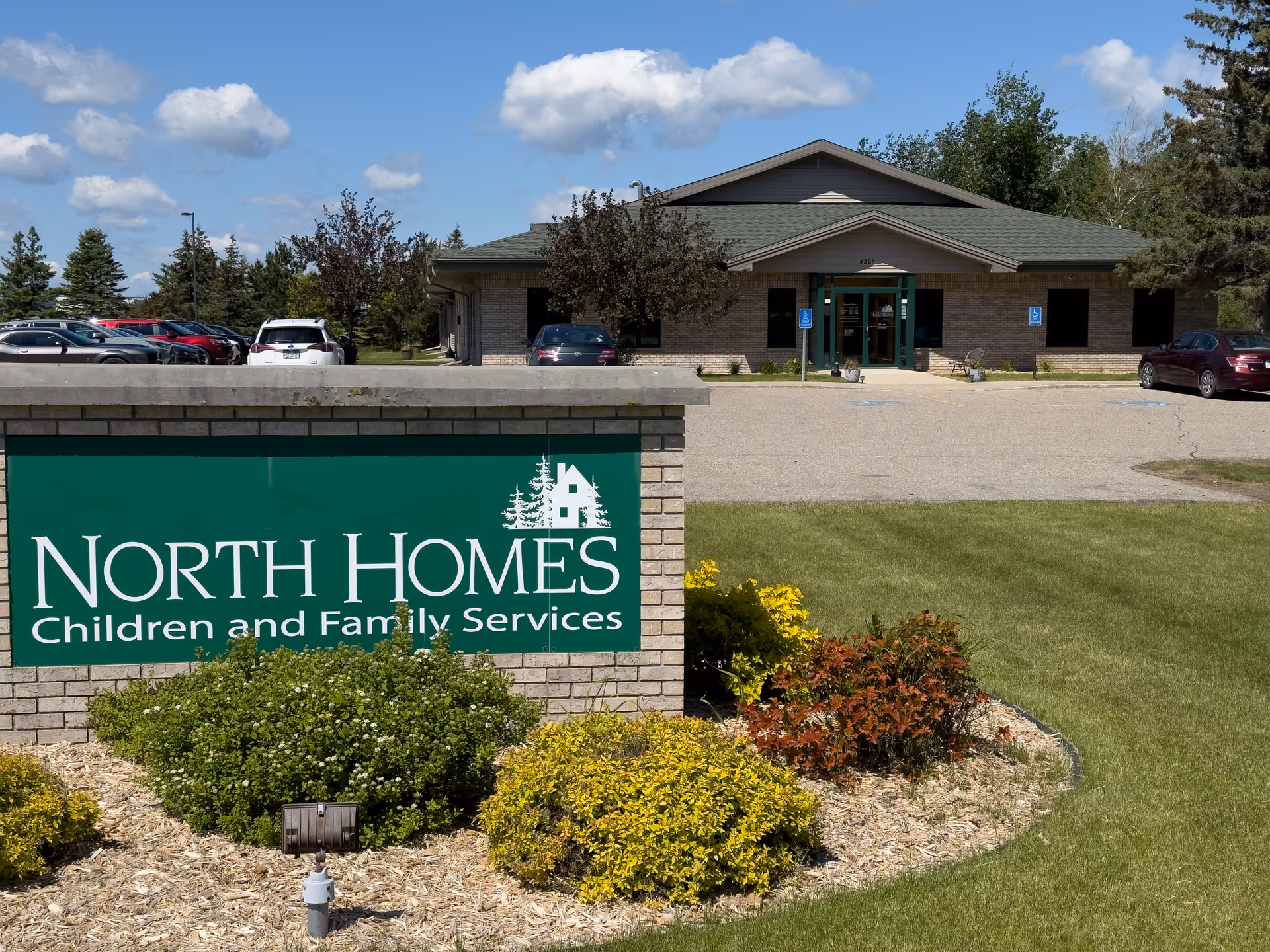 Exterior view of North Homes facility with green sign, parking lot, and landscaped entrance.